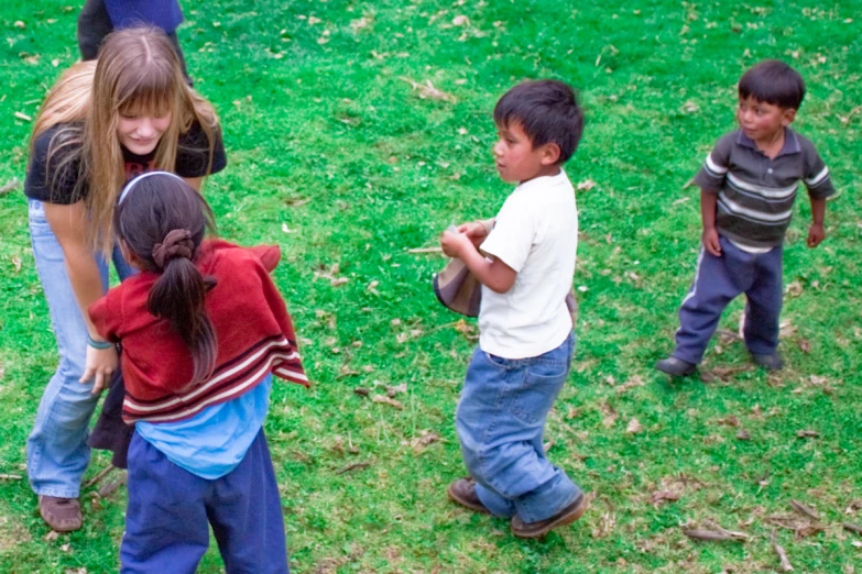 a woman holding a handbag with three young children standing in the grass