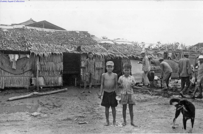 black and white pograph of boys standing in front of their huts with dogs