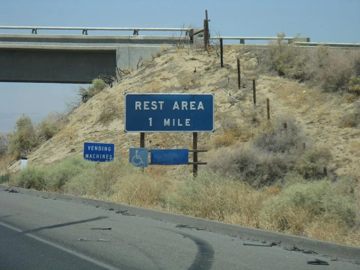 some signs that are by a highway with a hill