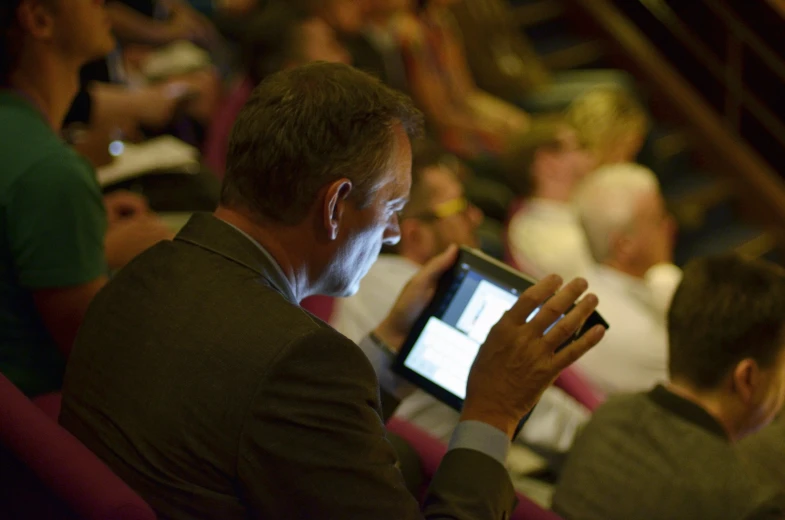 man playing on an electronic device while in a crowded auditorium