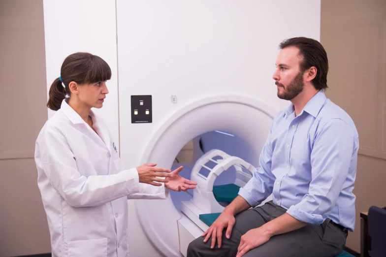 a man and woman in white shirts look into a mri