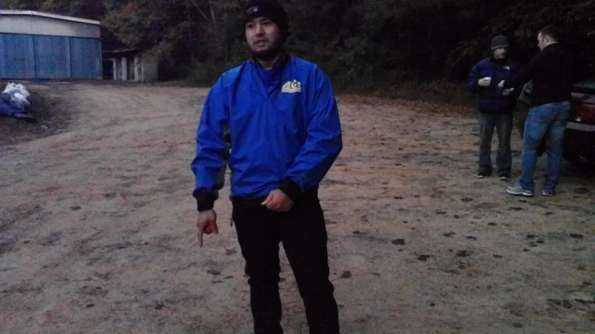 man holding an umbrella standing on dirt road in front of parked cars