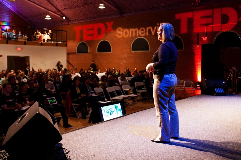 a female in a black top and jeans stands on a stage