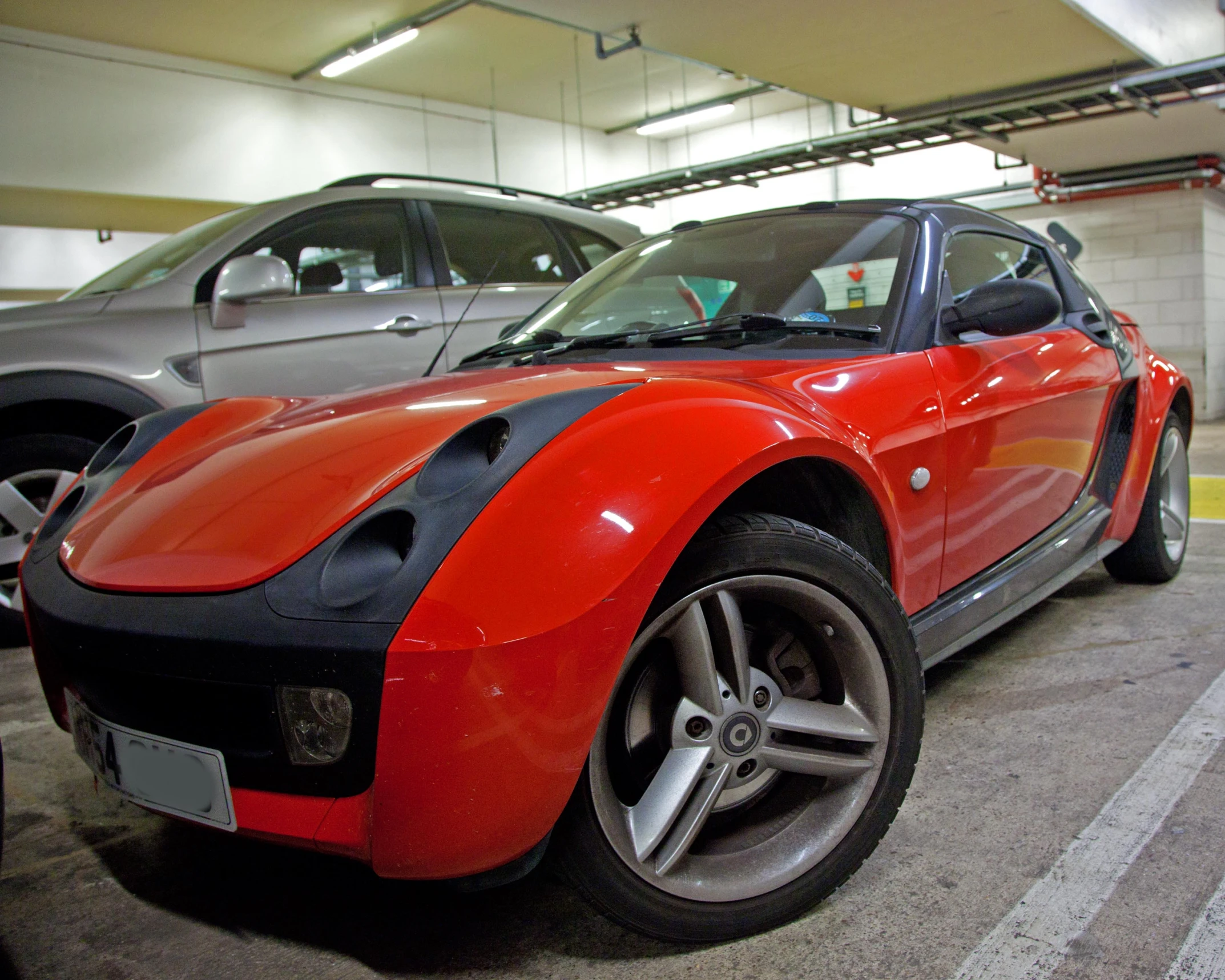 two cars parked in a garage, one red and the other black