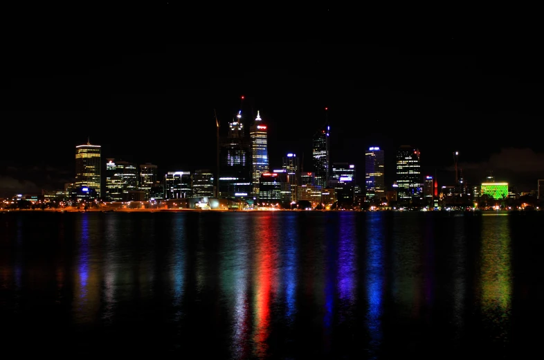 the city lights reflect in the water in a darkened area