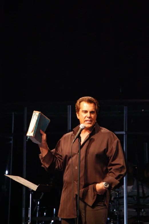 a man in brown stands next to a microphone while holding his book