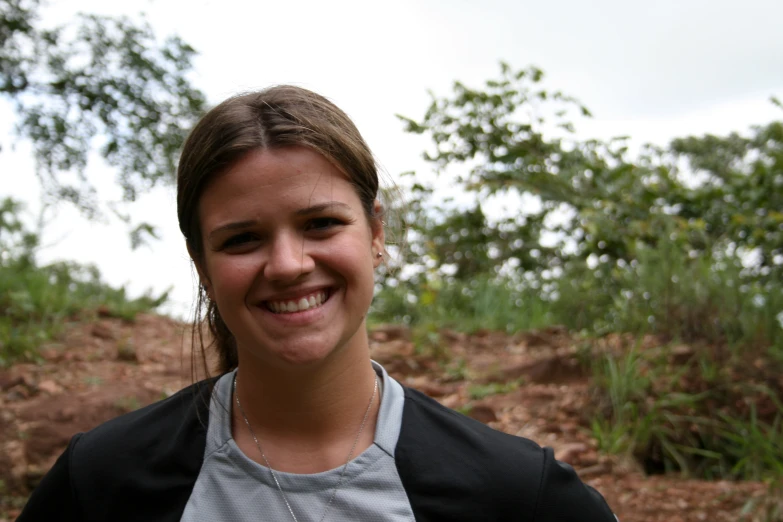 a woman in a jacket smiles in front of a wooded area