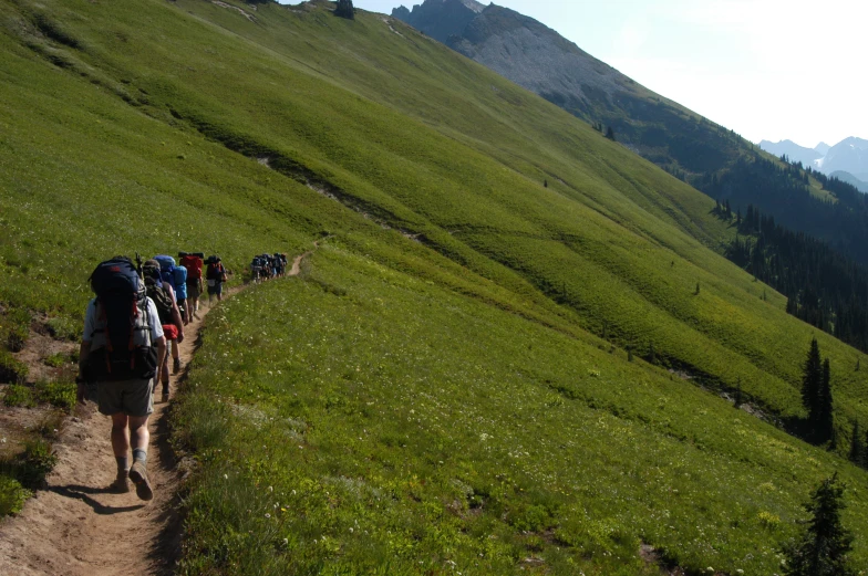 a number of people with backpacks hiking up a hill