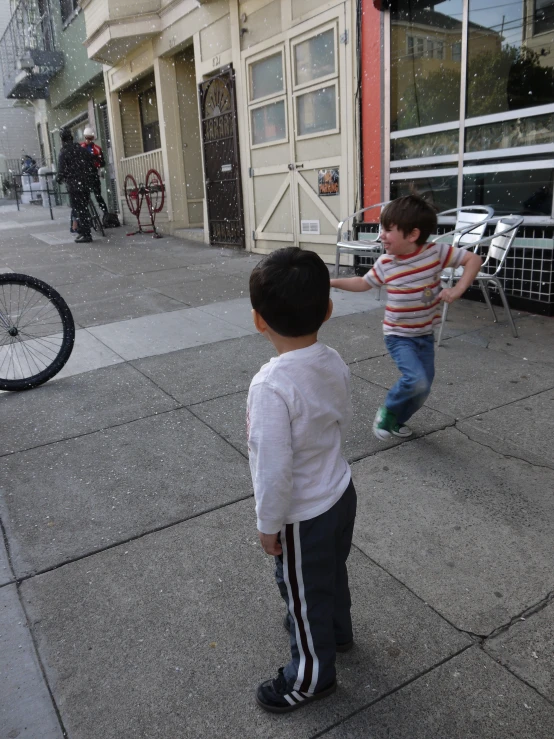 two young children playing on a city sidewalk