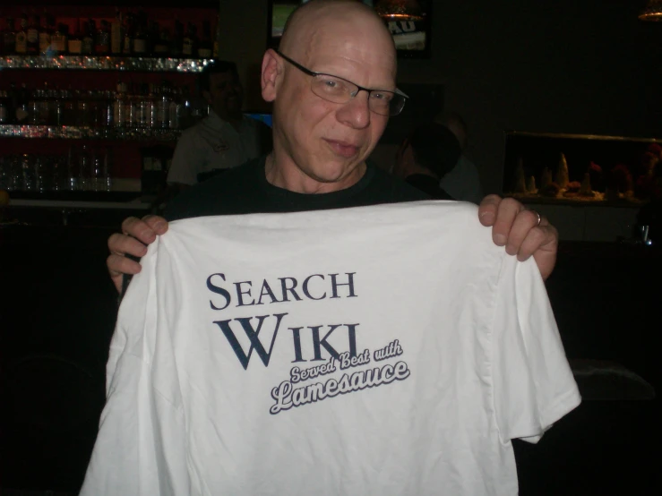 a man holding a white t - shirt that reads search wiki and someones sentence