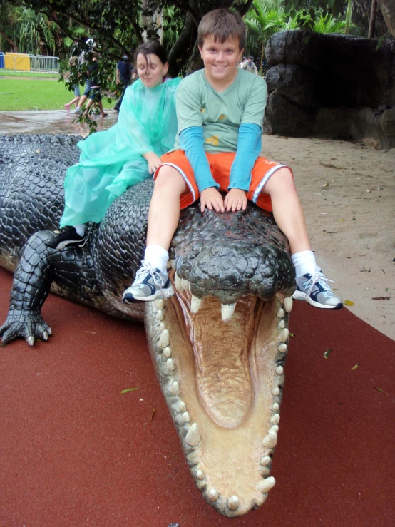 two s ride on an alligator statue at a park