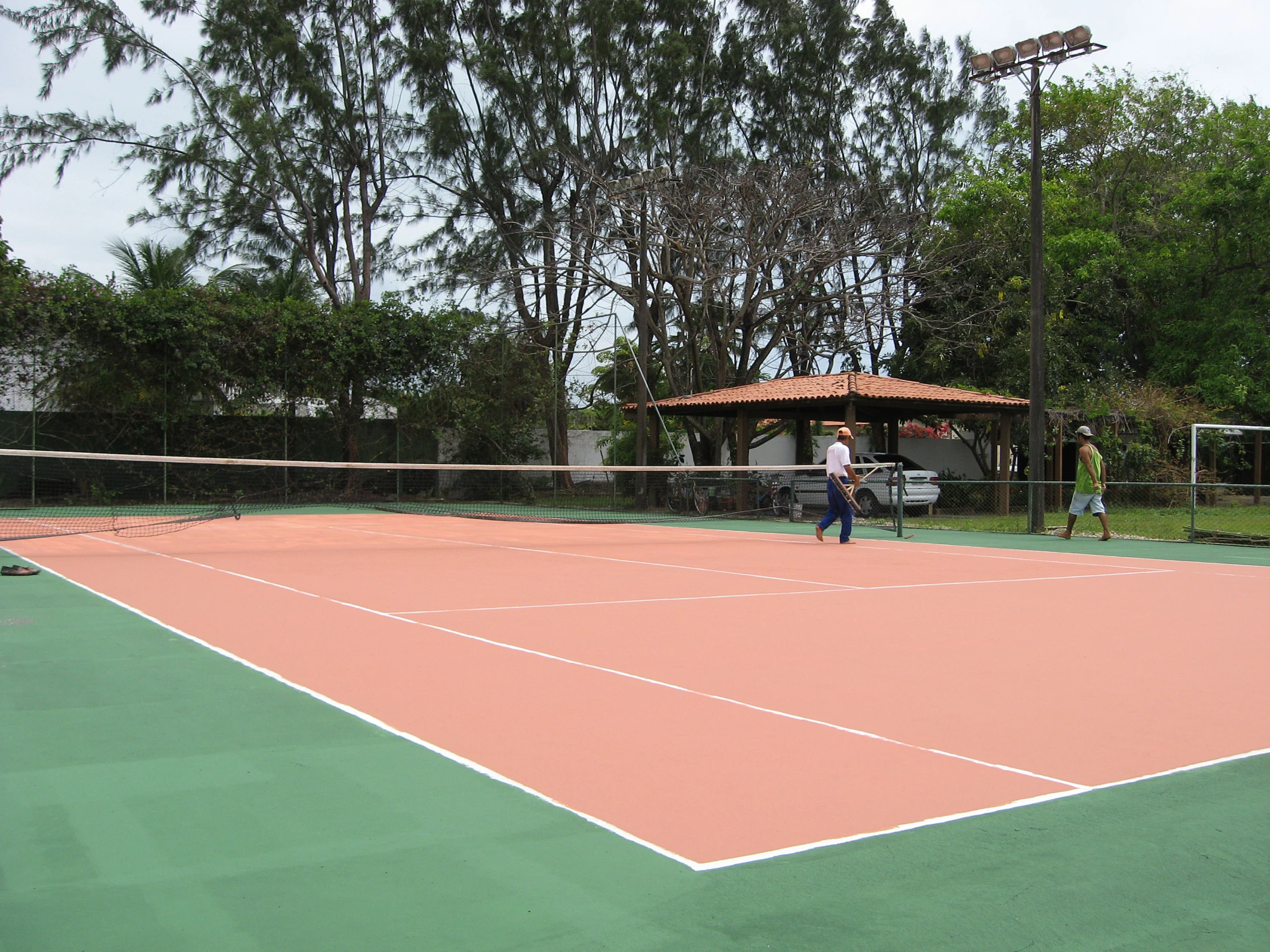 two people playing tennis on a court surrounded by trees