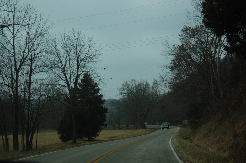 a road is deserted as a vehicle drives past on a cloudy day