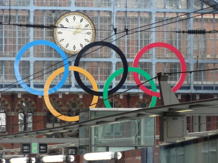 a clock with some rings is hanging in front of the olympic rings