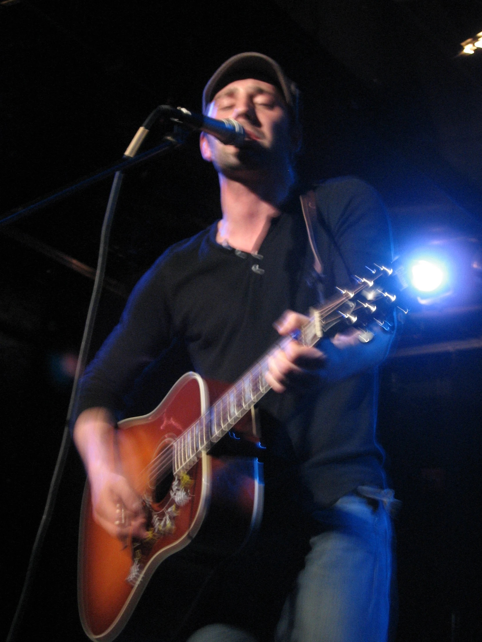 man with guitar in front of microphone in dark area