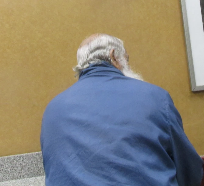 an elderly man sitting down wearing a blue shirt
