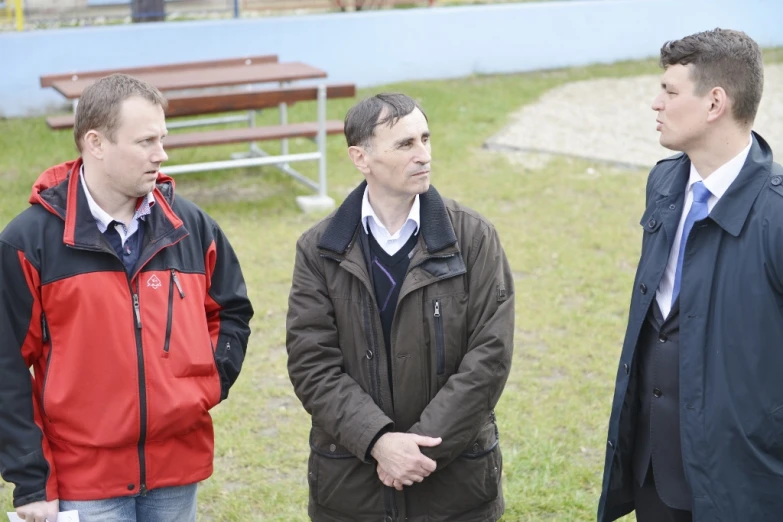 three men in jackets are having a discussion outdoors