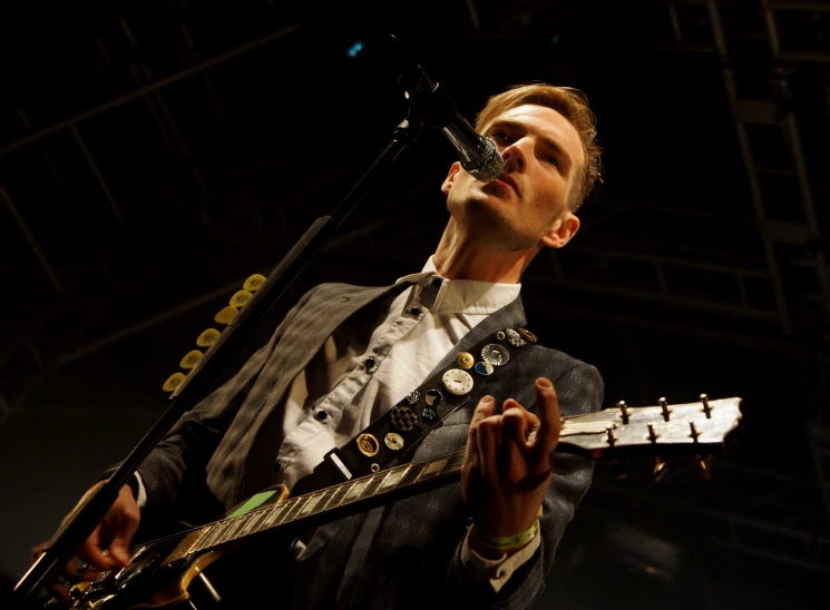 a young man with a guitar sings into the microphone