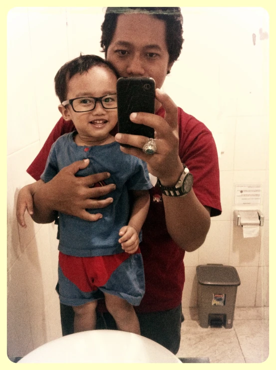 a  is holding his father while taking a selfie in the bathroom