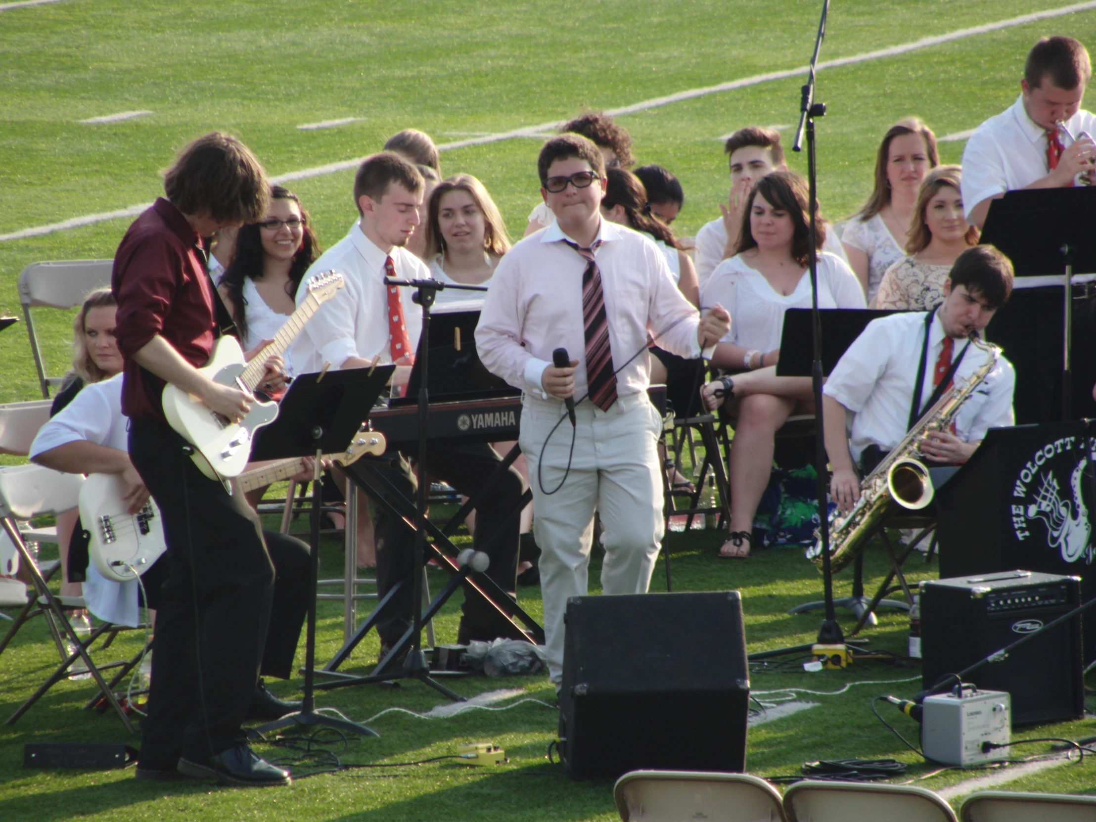 a group of people sitting around while a man in a tie sings into a microphone