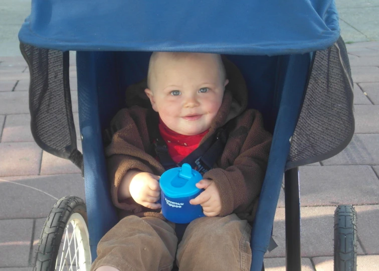 a child with a blue sippy cup in his hand is sitting in the stroller