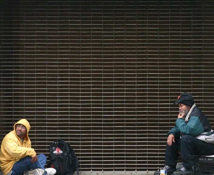two men are sitting on a bench talking on the phone