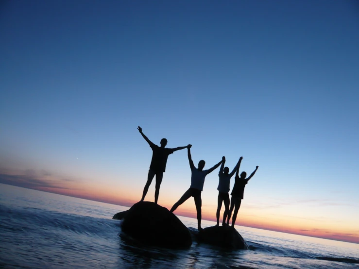 three men standing on some rocks in the water