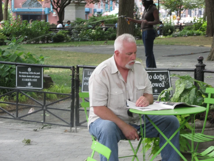 a man reading a paper at a green park table with green chairs