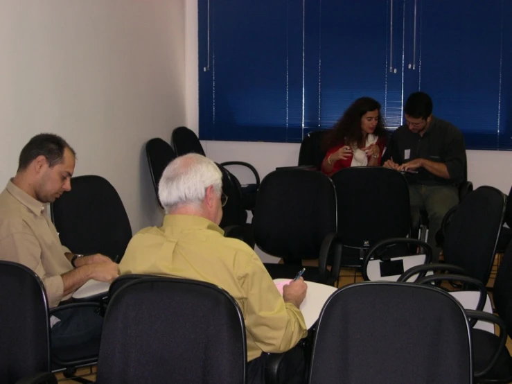four people sitting in an office with a few looking at their electronic devices
