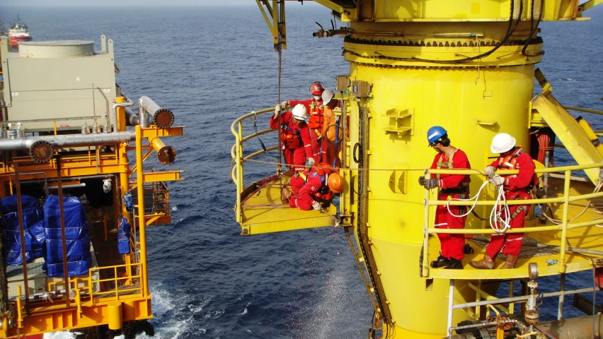 workers in orange and blue safety suits are climbing the deck of a large vessel