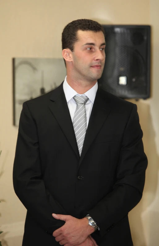 a young man in business clothes standing with his arms folded in his pockets