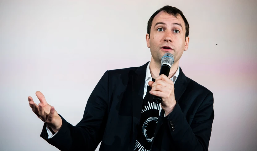 man in black suit with microphone and no expression