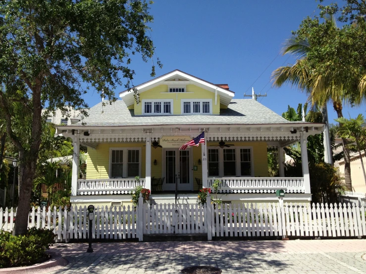 a yellow home with white picket fence and a small flag hanging