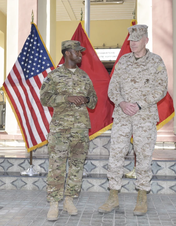 two soldiers stand with arms folded in front of flags