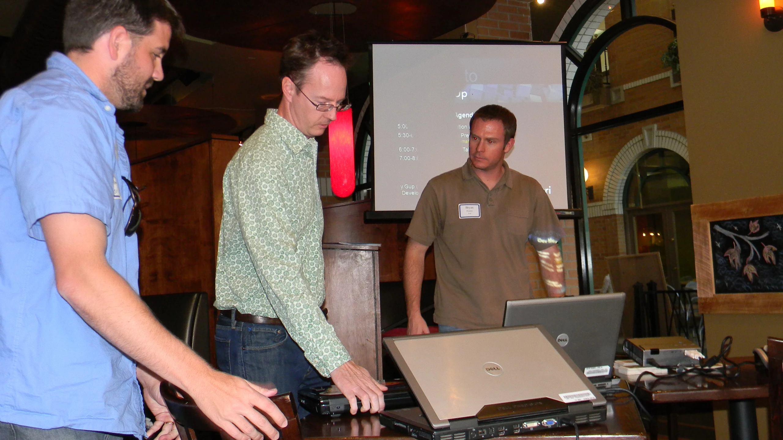 three men standing around talking in front of a projector screen