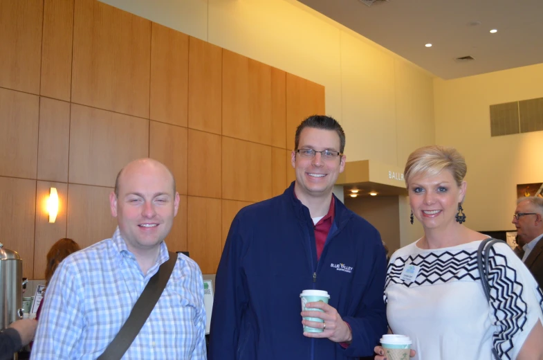 three people standing next to each other holding coffee cups