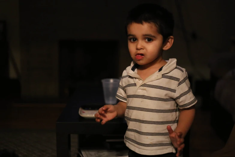 a small boy with one hand out while wearing a striped shirt