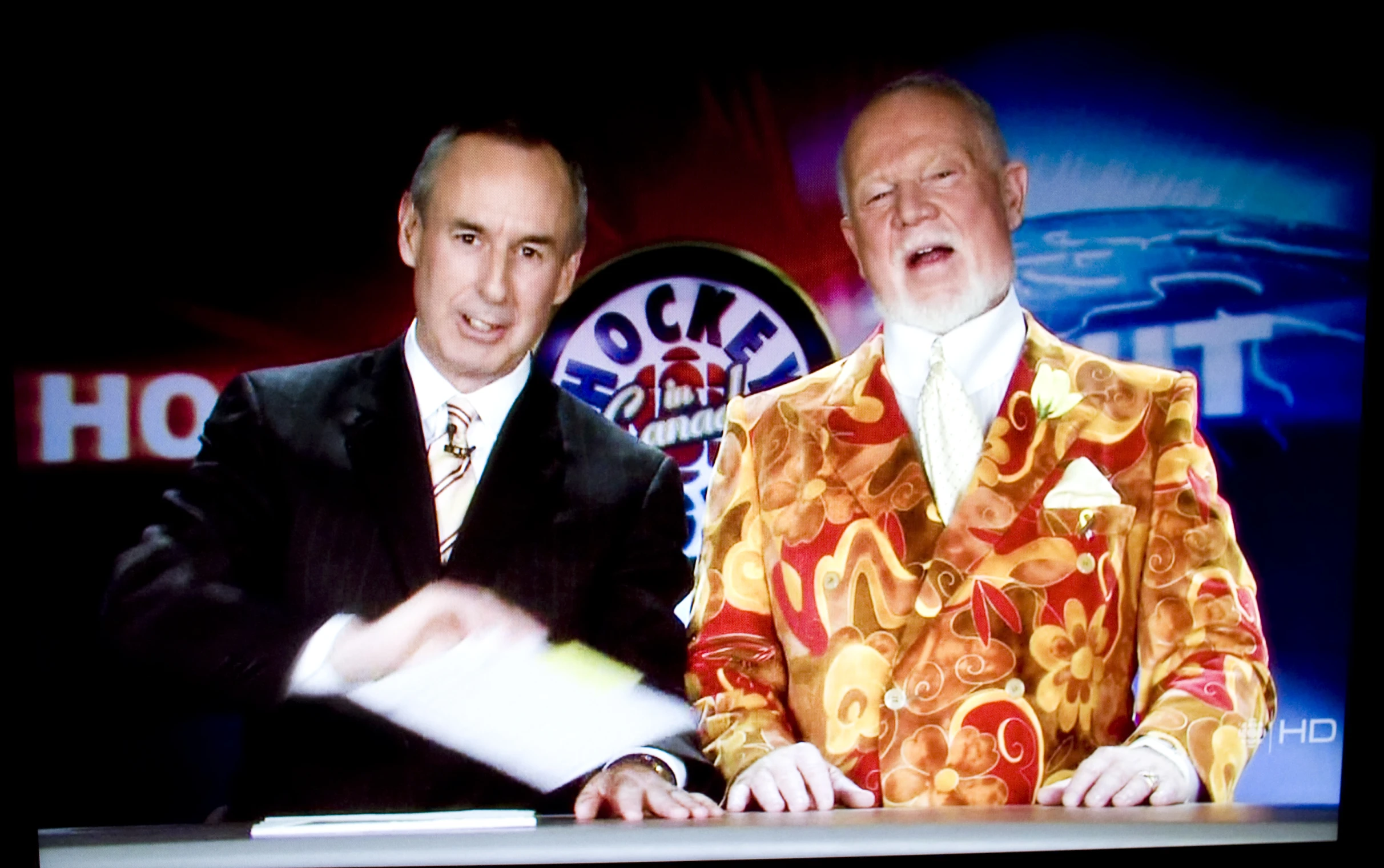 two men in colorful clothing stand in front of a television