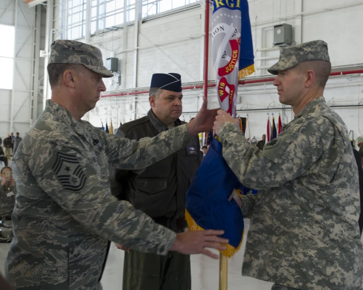 four men in uniform are at a ceremony holding a blue and white flag