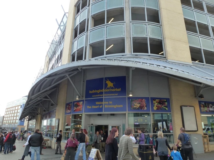 a large group of people walk near a building with lots of windows