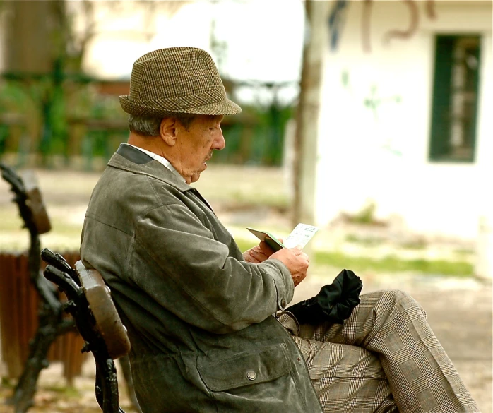 an old man sits outside on a bench reading a paper