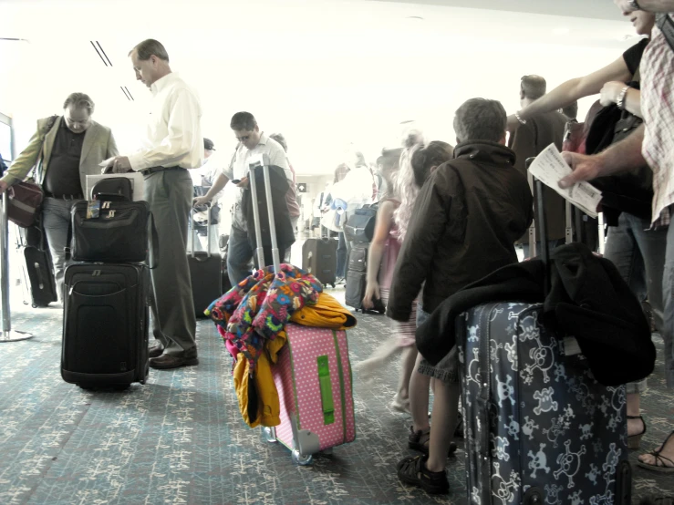 people wait with luggage in a large group