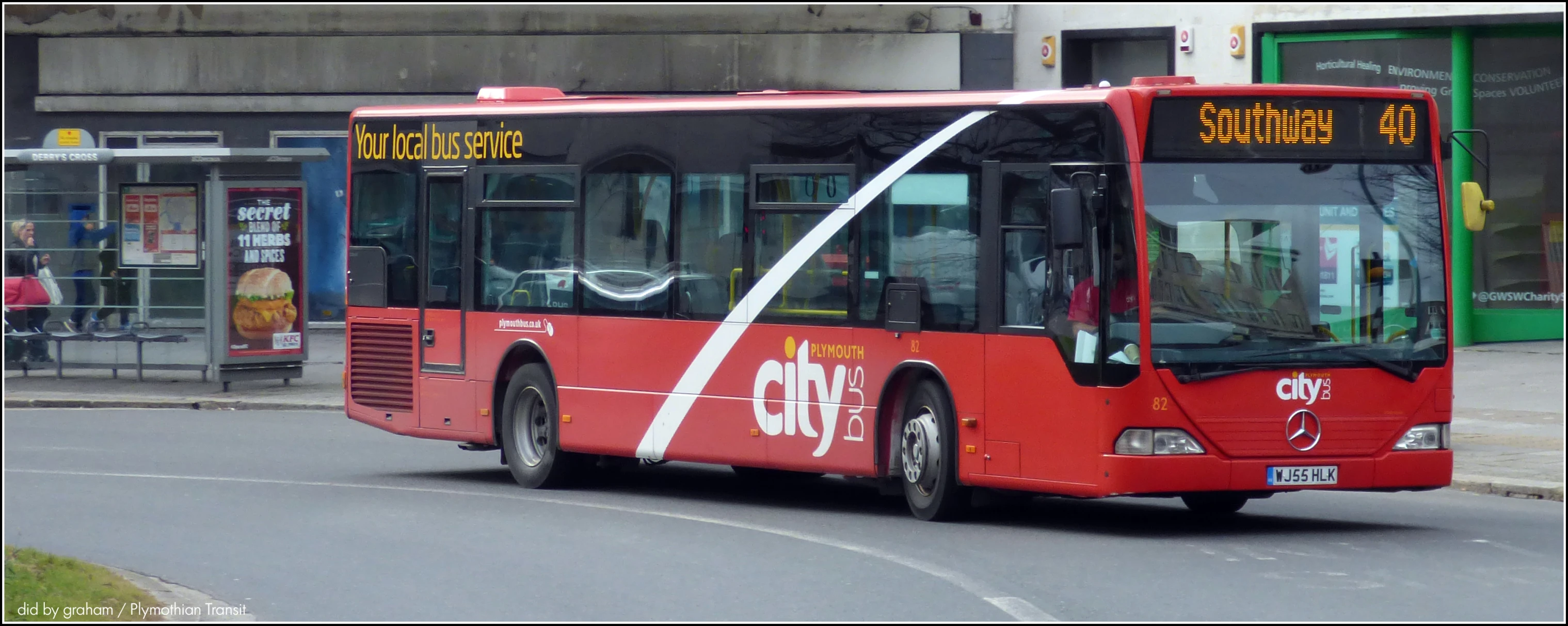 a red bus is on a street by a building