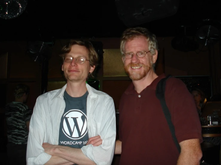 two men standing together holding up a logo t shirt