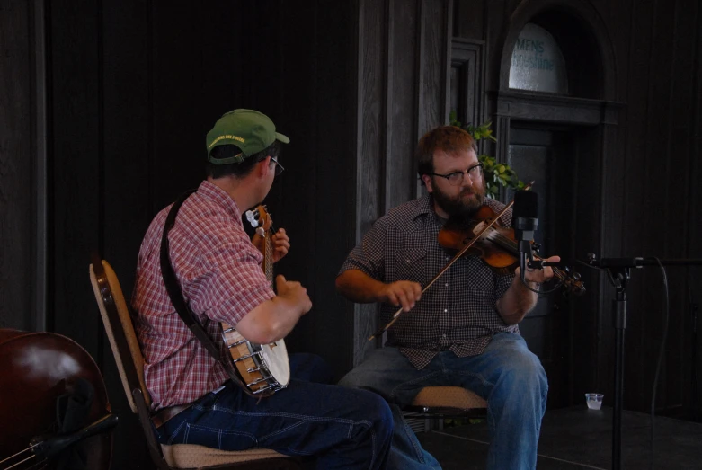 two men with guitars sitting in chairs playing music