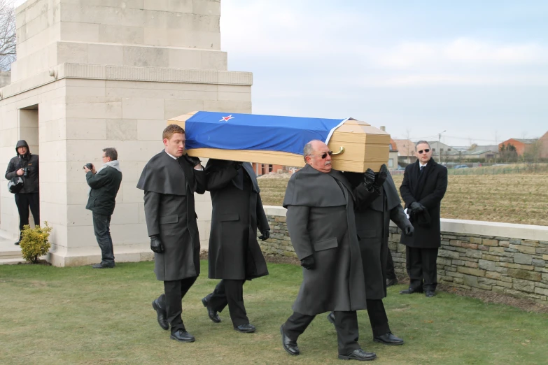 several people carrying a casket while others stand around