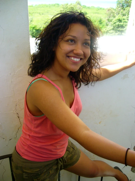 a smiling girl standing by a wall with her hand on her arm