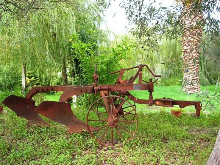 an old rusted farm plow sitting in the grass