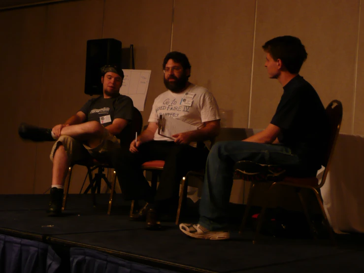 three guys sit in chairs at a paneled paneled room