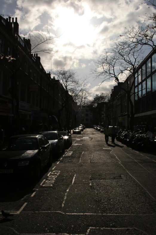 sun peeking through the clouds over a street lined with cars